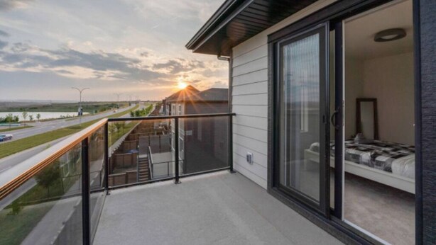 A balcony with a glass door leading to a bedroom with a bed and a nightstand. - Modern 3BR Townhome in Seton with Garage + Balcony (Calgary)