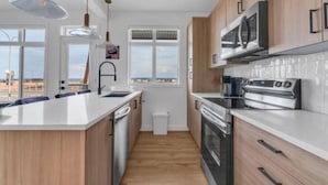 A modern kitchen with wooden cabinets, stainless steel appliances, and a large island. - Modern 3BR Townhome in Seton with Garage + Balcony (Calgary)