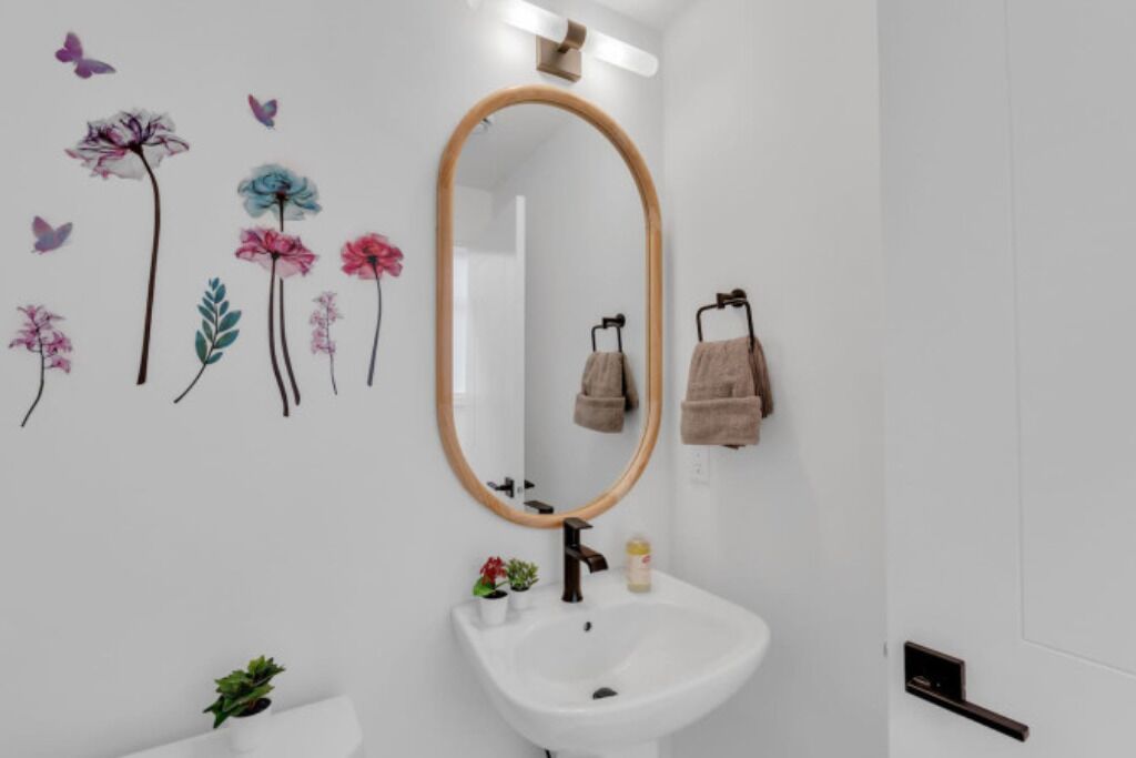 A bathroom with a white sink, a mirror with a wooden frame, and decorative wall stickers of flowers and butterflies.