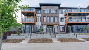 A modern multi-story residential building with balconies, a central entrance, and a landscaped front yard. - Modern 3BR Townhome in Seton with Garage + Balcony (Calgary)