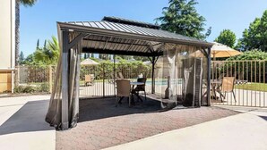 Un espacio de estar al aire libre cubierto con una mesa y sillas, rodeado de una valla y árboles.