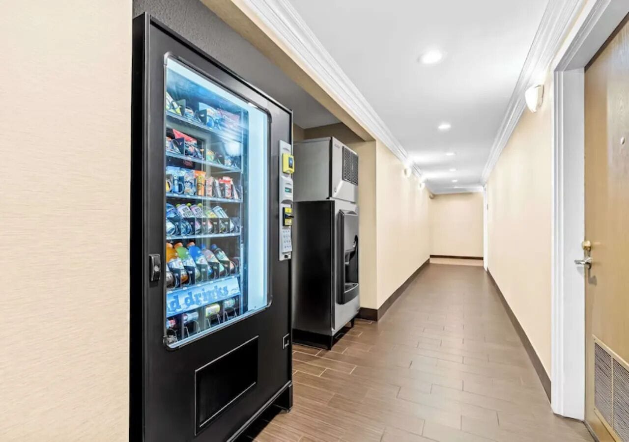 A hallway with a vending machine stocked with drinks and a microwave.
