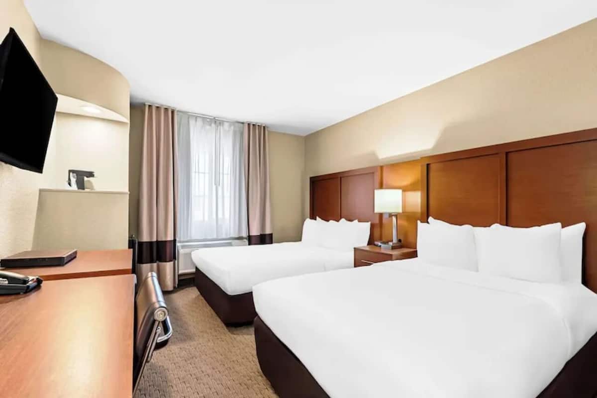 A hotel room with two beds, a desk, a TV, and a window with curtains.