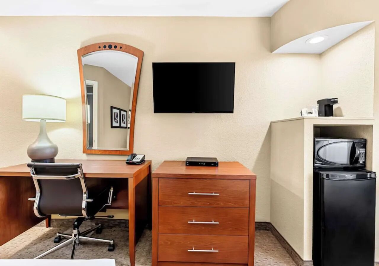 Habitación de hotel con escritorio, silla, cómoda, espejo, televisor, microondas y refrigerador.