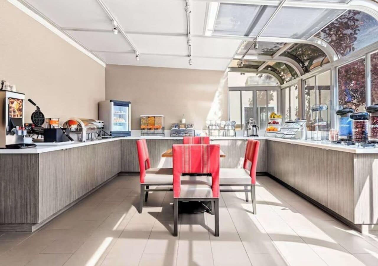 A modern kitchen with a central island, red chairs, and a glass enclosure.