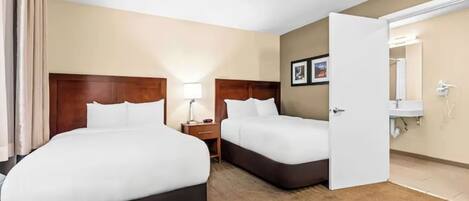 A hotel room with two beds, a nightstand, a lamp, a bathroom with a sink and mirror, and a door leading to another room.
