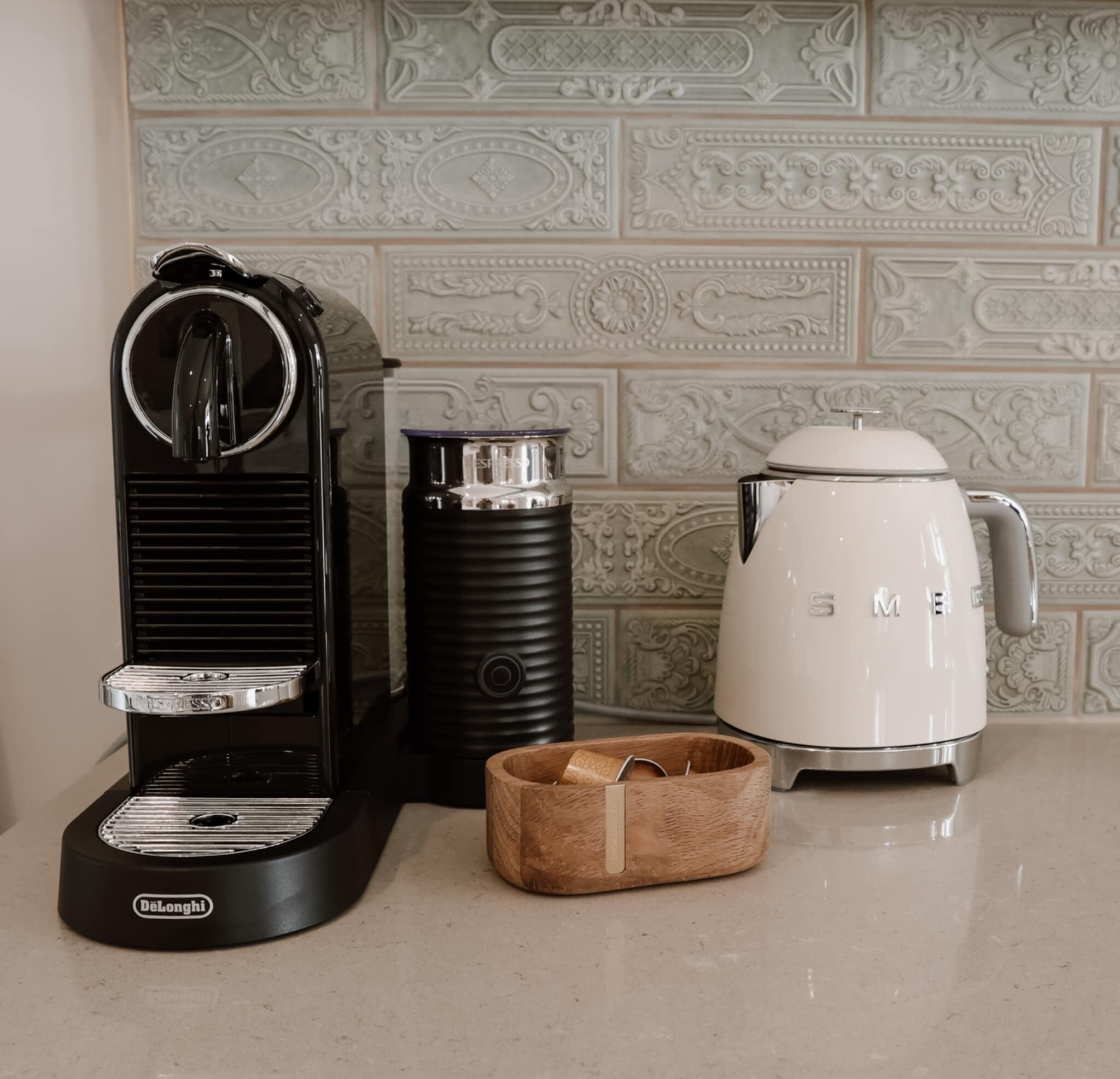 Una cafetera, un hervidor y una jarra de café sobre una encimera con baldosas decorativas al fondo.