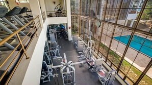 Een sportschool met loopbanden, krachttoestellen en een zwembad, zichtbaar door grote ramen.