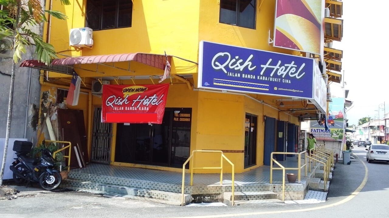 A hotel named Qish Hotel with a yellow facade and a red banner advertising a new opening.