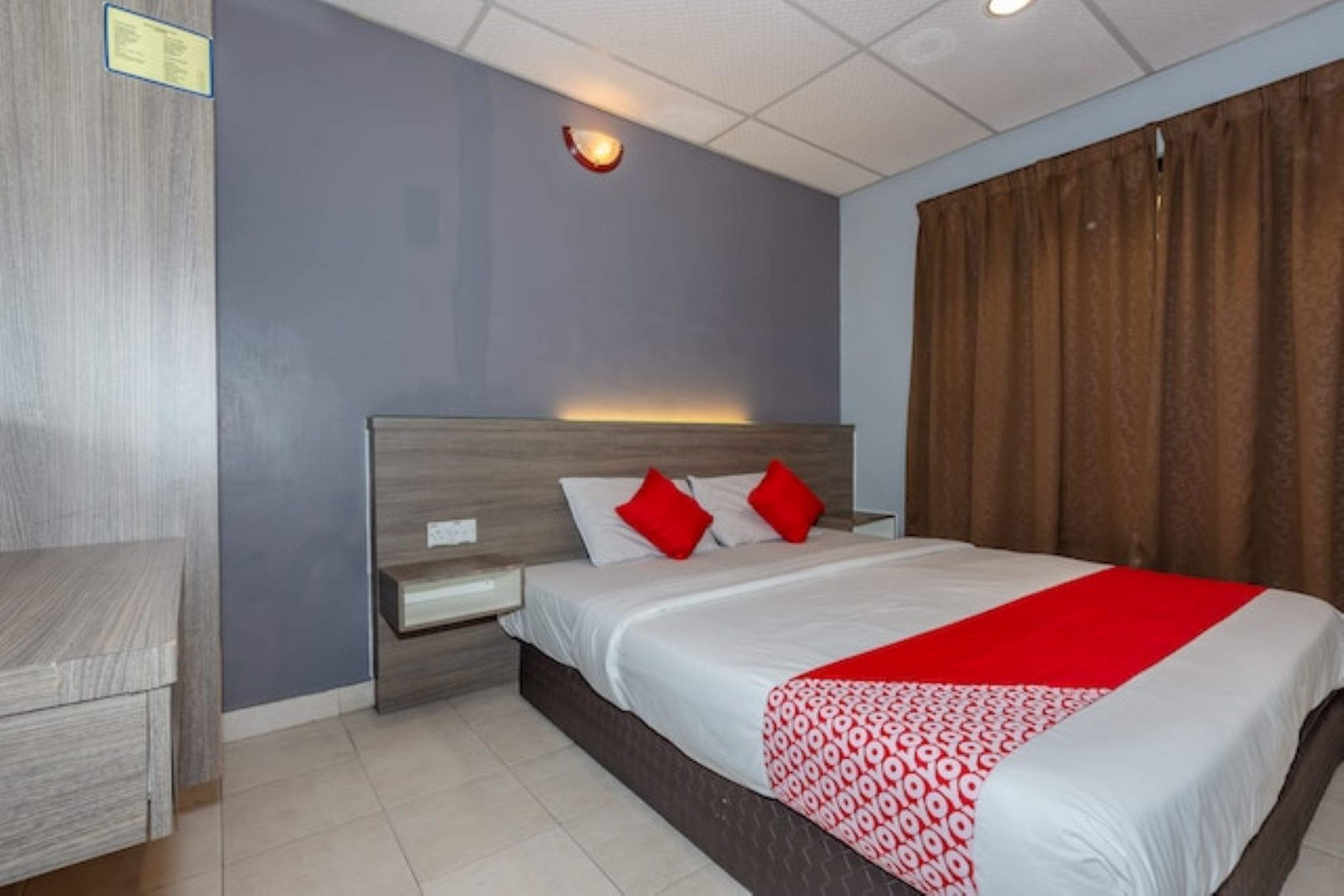 Una habitación de hotel con una cama, una mesita de noche, un cabecero de madera y un ventanal con cortinas.