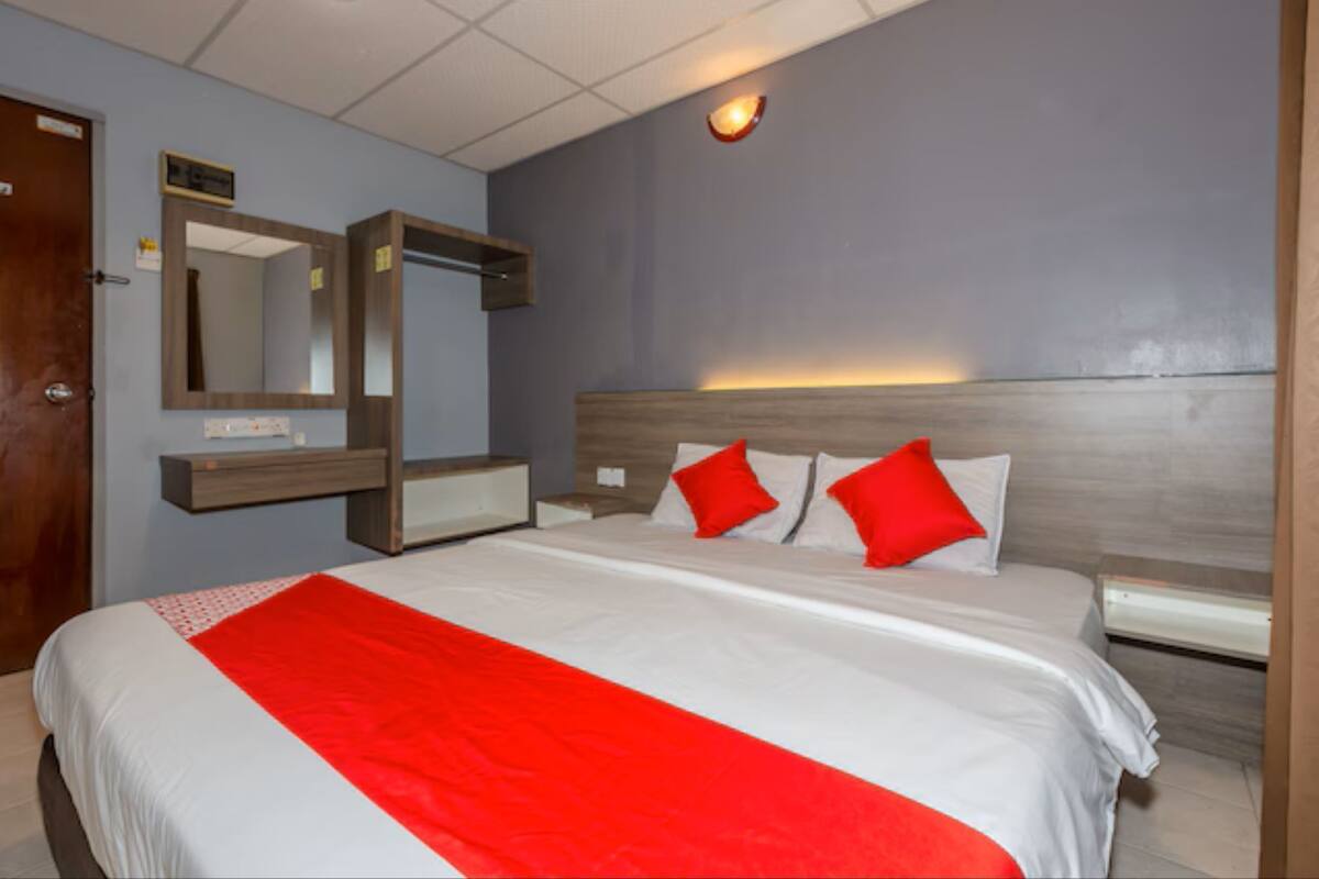 Hotellihuone, jossa on suuri sänky, puinen pääty ja punavalkoinen päiväpeite.