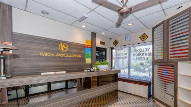 A reception area with a reception desk, a ceiling fan, and a window with a view of the outside. - Hotel Q Banda Kaba (Malacca City)