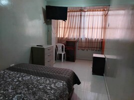 Un dormitorio con cama, escritorio, silla, televisor y armario.