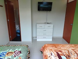 Un dormitorio con dos camas, un aparador blanco, un televisor en la pared y la puerta de un baño a la vista.
