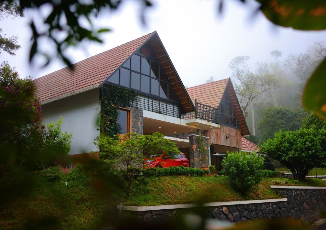 A modern house with a sloped roof, large windows, and a red car parked in front.