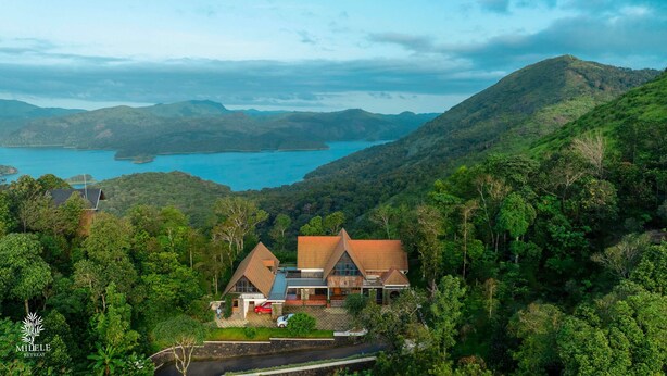 Une maison avec un toit en pente, entourée d’une végétation luxuriante et offrant une vue sur un lac.