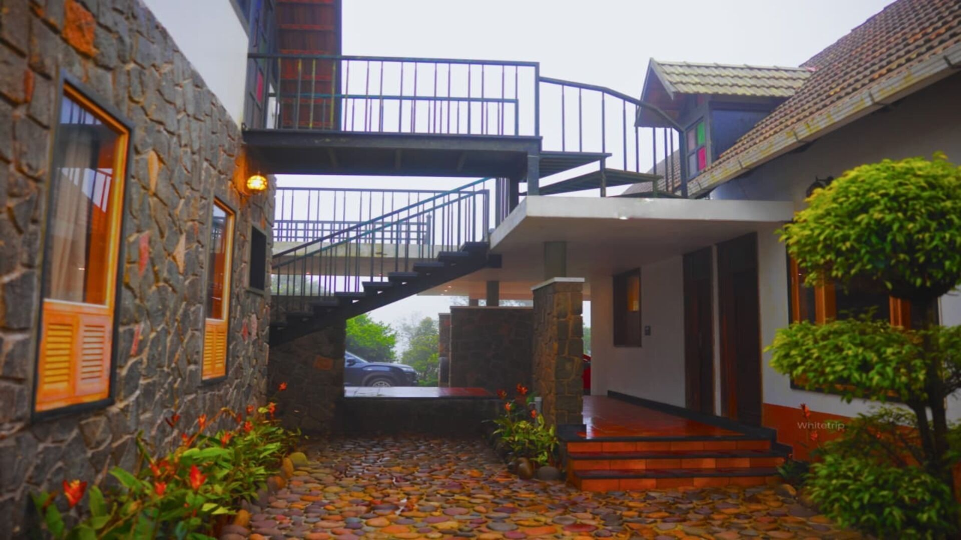 A stone building with a balcony, a staircase, and a paved pathway with flowers.