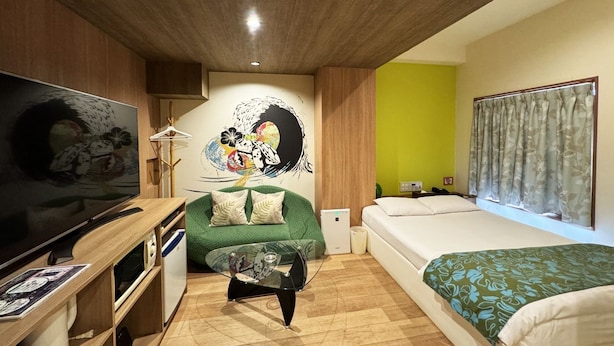 A room with a television, a green sofa, a bed, and a wall mural. - Hotel La'i Laurel (Tokyo)