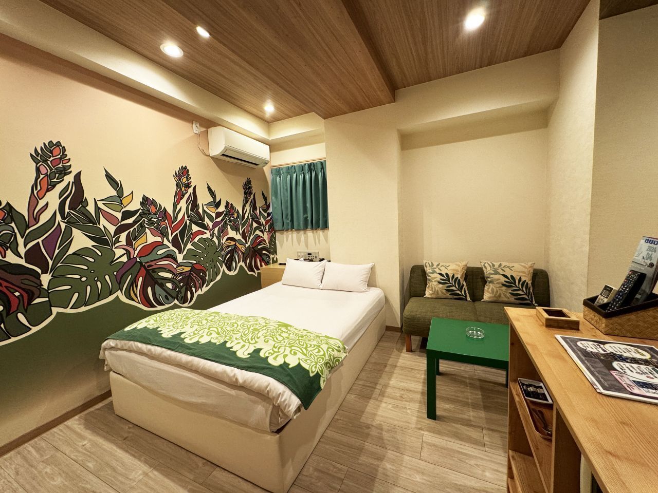 Une chambre d’hôtel avec un lit, un canapé vert, un bureau en bois et une fresque murale.