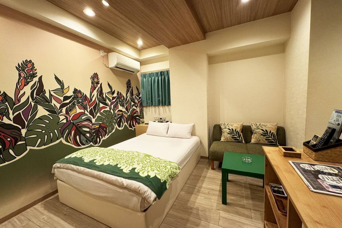 A hotel room with a bed, a green sofa, a wooden desk, and a wall mural.
