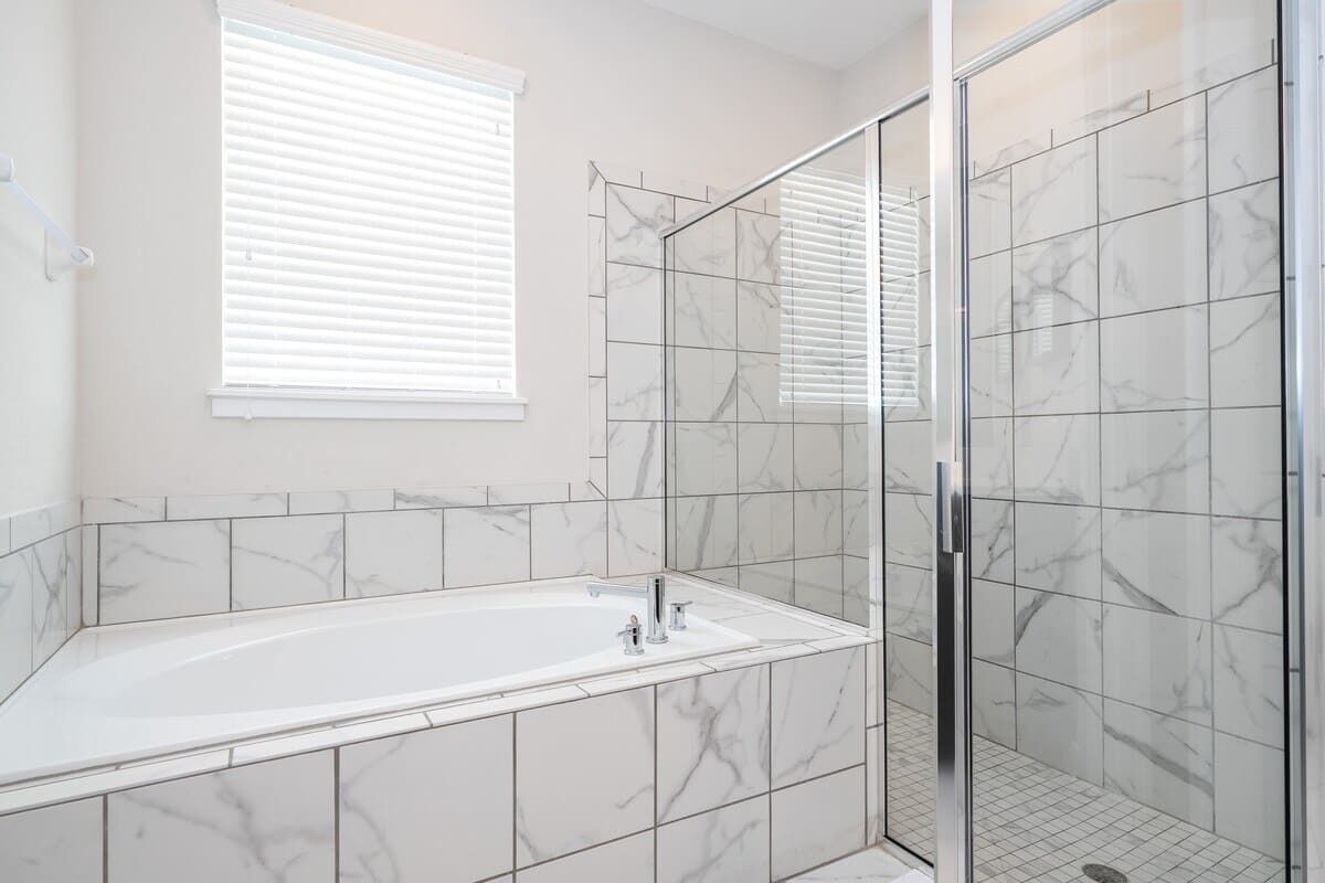 A bathroom with a bathtub, a glass shower enclosure, and a window with blinds.
