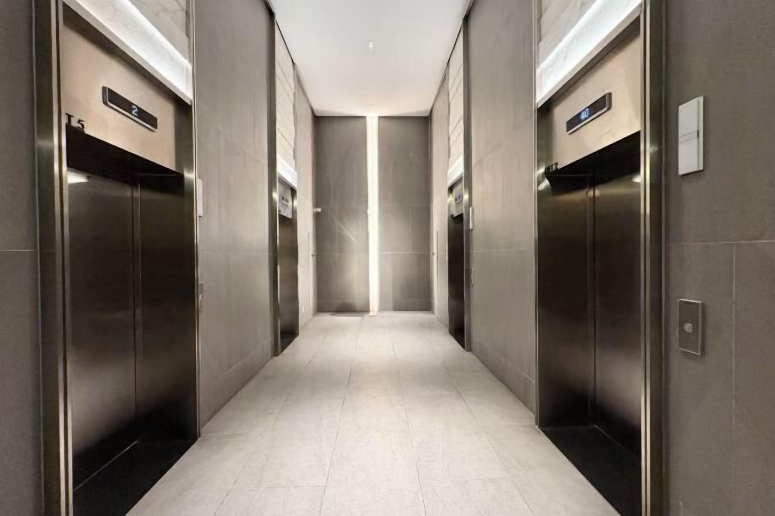 A modern elevator lobby with two elevators, a tiled floor, and a plain wall.