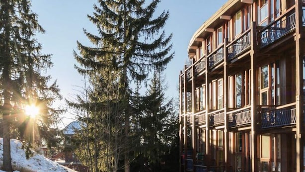 A multi-story building with balconies and large windows, surrounded by tall evergreen trees. - Holiday Home in Charmettoger Near Ski Lift (Bourg-Saint-Maurice)