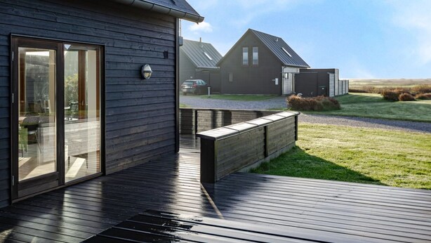 Een modern gebouw met grote glazen deuren, een houten terras en een metalen dak.
