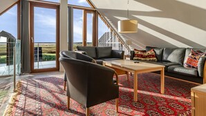 Een ruime kamer met een groot raam, een bank, een bijzettafeltje en een kamerkleed met dessin.