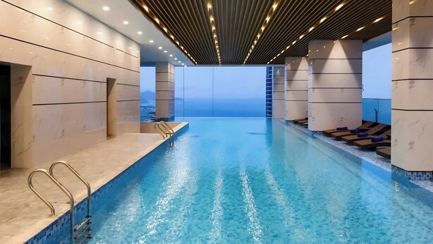 Une piscine intérieure moderne, avec une eau d’un bleu limpide, un plafond en lambris de bois et des murs en marbre.