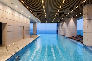 En moderne swimmingpool indendørs med klart, blåt vand, et træloftsloft og marmorvægge.