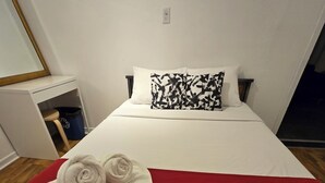 Hotellihuone, jossa on sänky, punainen heittopeitto, kaksi rullalle taitettua pyyhettä, valkoinen tyyny ja mustavalkoinen kuviollinen koristetyyny.
