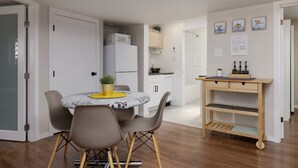 A compact kitchen with white cabinets, a microwave, and a small dining area with a round table and chairs. - Coho Trailside Comforts (Squamish)