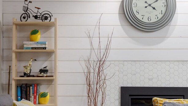 A living room with a fireplace, a round wall clock, a bookshelf, and two grey sofas. - Coho Trailside Comforts (Squamish)
