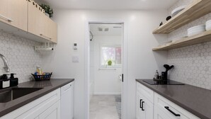 A modern kitchen with white cabinets, dark countertops, and a hexagonal tile backsplash. - Coho Trailside Comforts (Squamish)