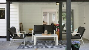 A covered porch with a white table, two chairs, and a patterned rug. - Coho Trailside Comforts (Squamish)