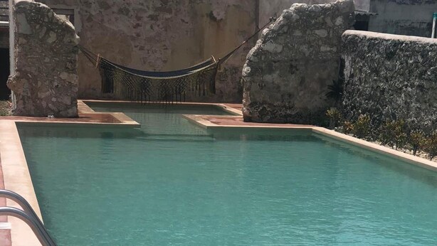 Una piscina rectangular con agua cristalina, rodeada de muros de piedra y una barrera de cuerda.