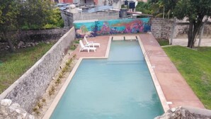 Una piscina rectangular con borde de piedra y un mural en la pared de fondo.