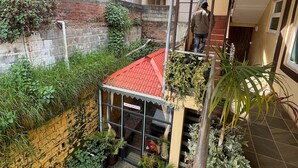 A courtyard with a red-roofed structure, a parked car, and various plants. - Essar Cottage (Ootacamund)