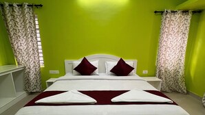 A neatly made bed with white linens and two red pillows, a white headboard, and a green wall with a ceiling light fixture. - Essar Cottage (Ootacamund)