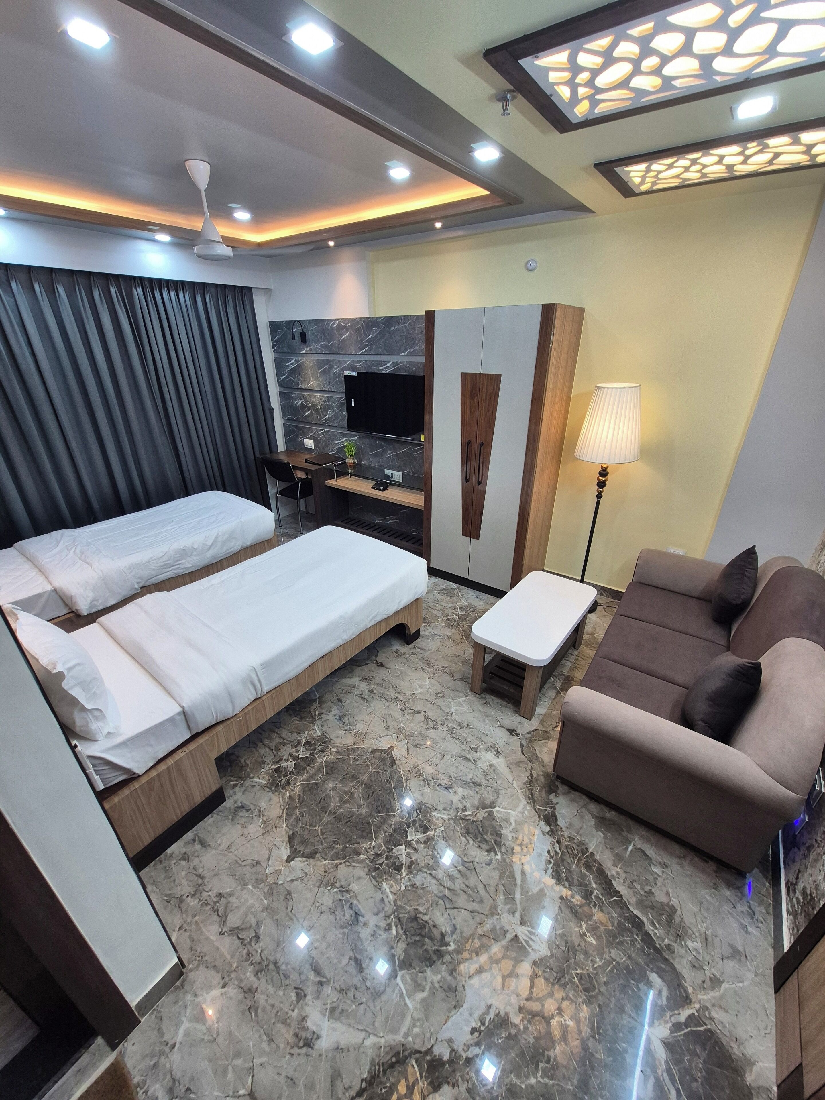 A modern hotel room with two single beds, a sofa, a desk, and a TV.
