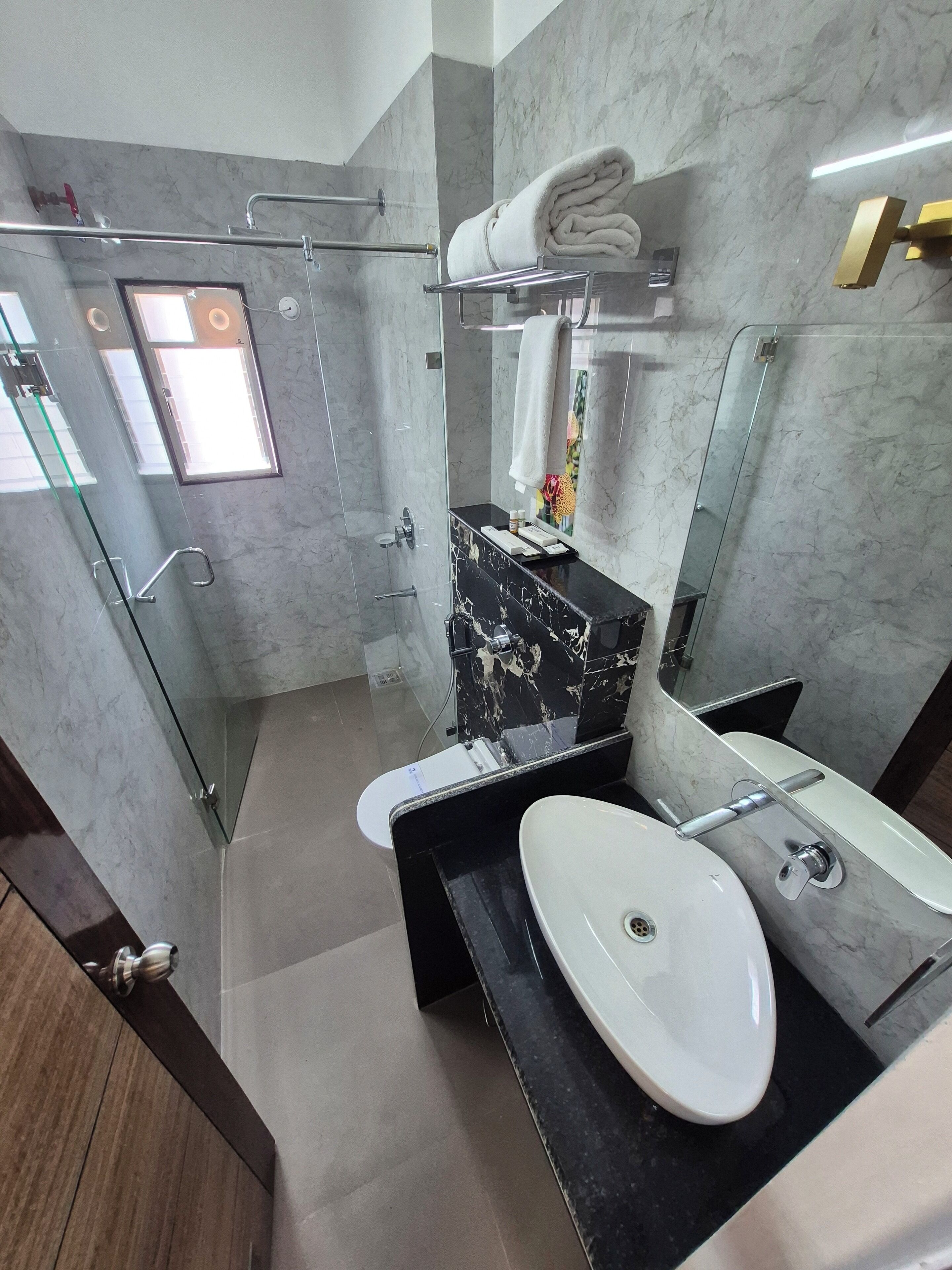 A modern bathroom with a glass shower enclosure, a marble vanity, a white sink, and a large mirror.
