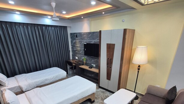 Una habitación de hotel con dos camas, un sofá, un escritorio, un televisor y una lámpara.
