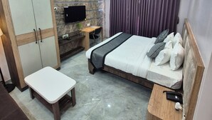 A modern hotel room with a bed, a desk, a wardrobe, and a TV. - Purnima International (Cooch Behar)