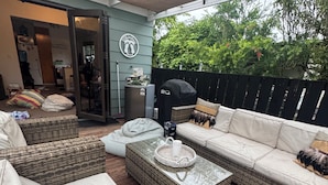 A covered outdoor seating area with wicker furniture, a barbecue grill, and a patio umbrella.