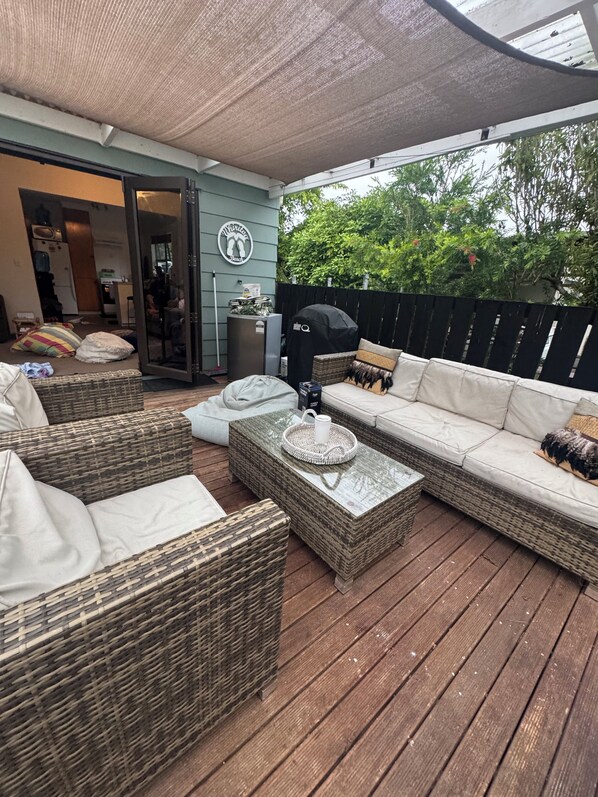 A covered outdoor seating area with wicker furniture, a barbecue grill, and a patio umbrella.