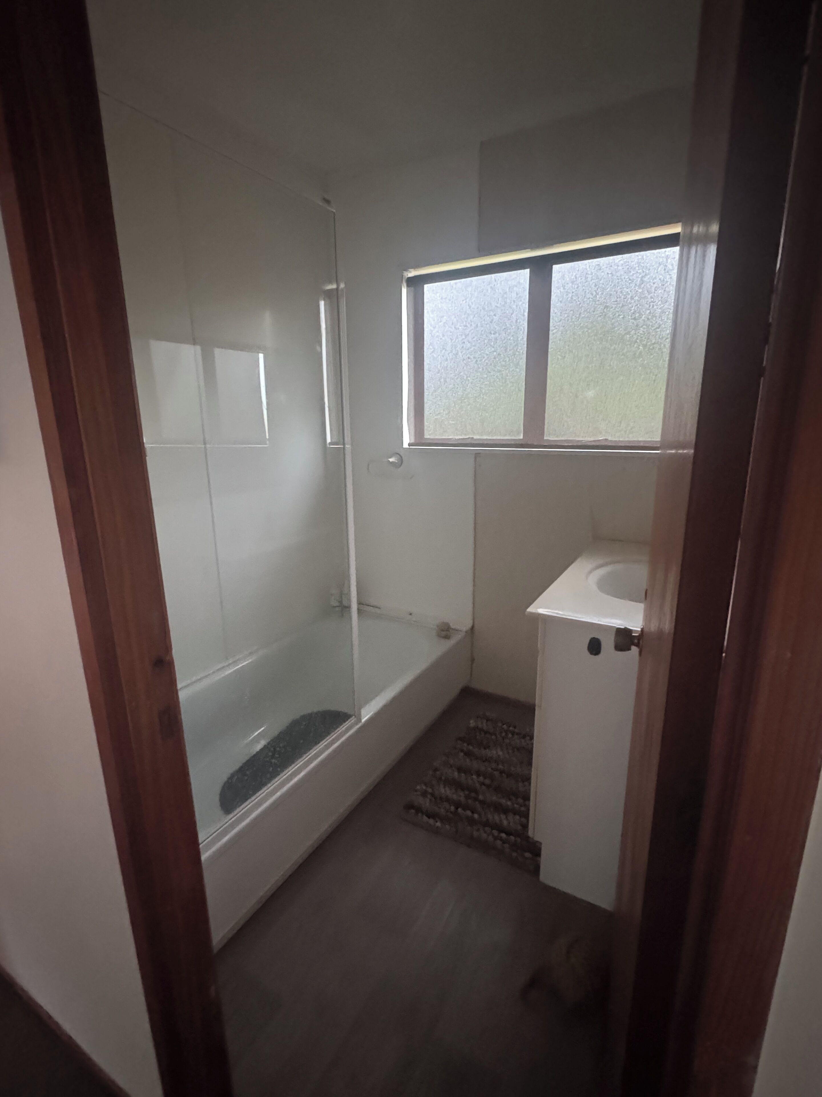 Un baño con ducha de vidrio, un lavabo blanco y una ventana pequeña.