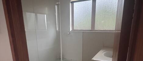 Un baño con ducha de vidrio, un lavabo blanco y una ventana pequeña.