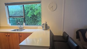 A compact kitchen with a window, sink, and a clock on the wall.