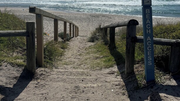 A wooden staircase leading to a beach with a sign reading "BEACH ACCESS".
